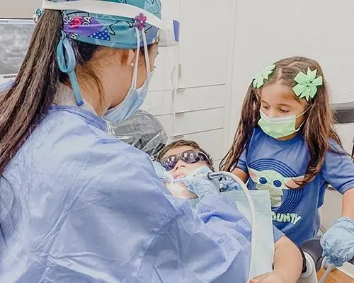Best dentist in Tamarac, FL performing dental procedures on patient with child watching from the side